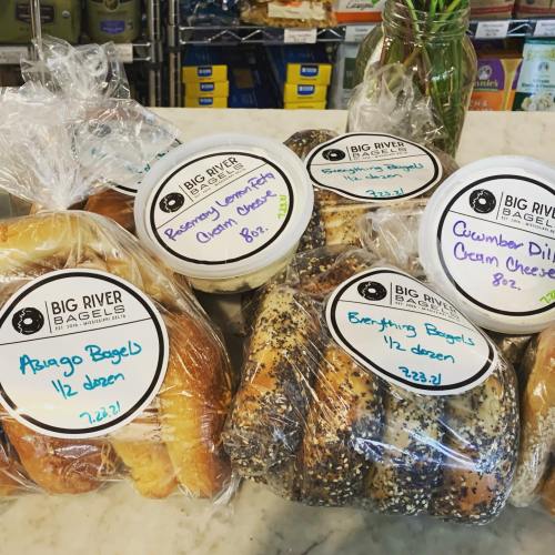 A variety of bagels in clear packaging, labeled with flavors and prices, displayed on a countertop.