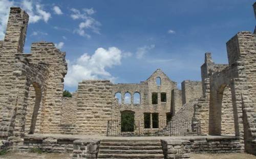 Ruins of a stone building with arched windows under a blue sky with scattered clouds.