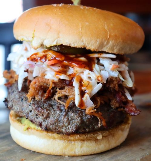 A towering burger with a beef patty, pulled pork, coleslaw, and barbecue sauce, all in a soft bun.