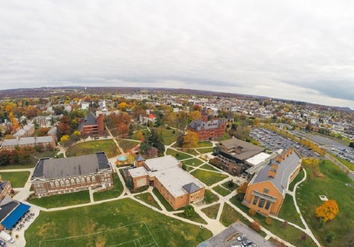 Aerial view of a college campus surrounded by trees with autumn foliage and nearby buildings and parking areas.