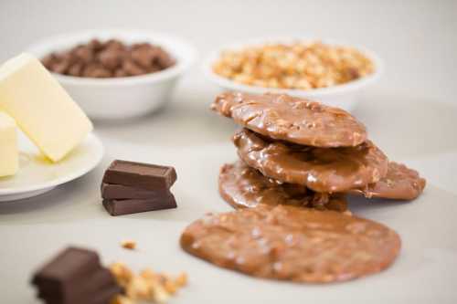 A stack of chocolate discs with butter, chocolate chips, and granola in the background on a light surface.