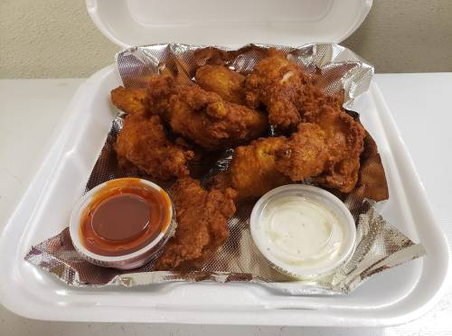 A takeout container filled with crispy fried chicken wings and two dipping sauces, one red and one white.