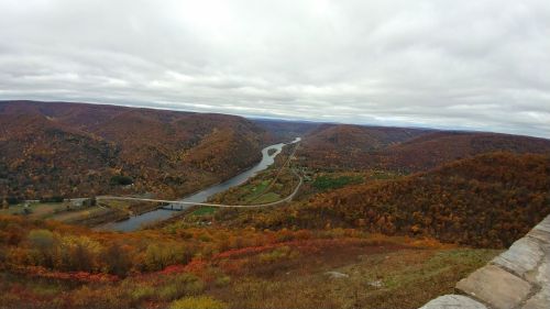 A scenic view of rolling hills with autumn foliage and a winding river below under a cloudy sky.