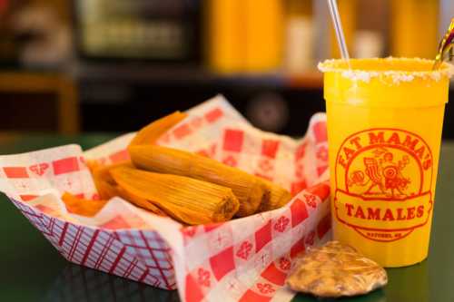 A basket of tamales next to a yellow cup with a festive drink, all set on a colorful table.