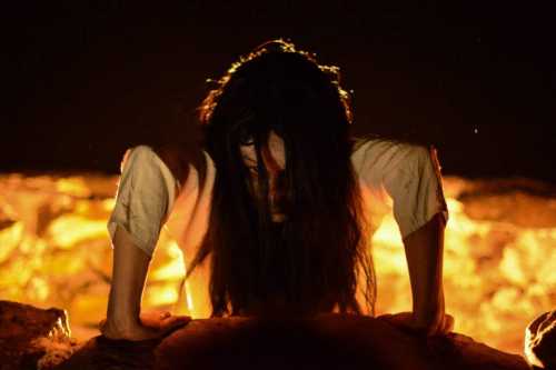 A figure with long dark hair crawls ominously towards the viewer, illuminated by a fiery glow in the background.