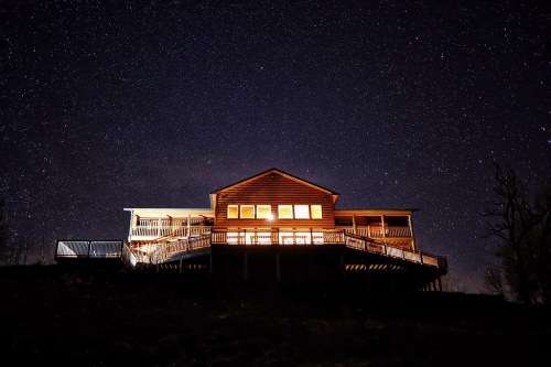 A wooden house illuminated at night, set against a starry sky.