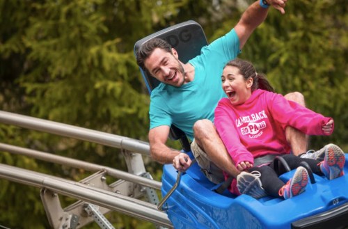 A man and a woman joyfully ride a roller coaster, both smiling and enjoying the thrill of the ride.