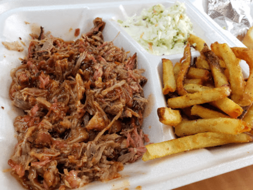 A takeout container with pulled pork, coleslaw, and crispy French fries.