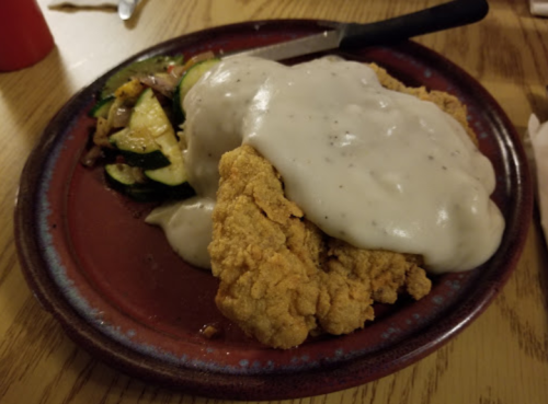 A plate of fried chicken smothered in white gravy, served with sautéed vegetables on the side.