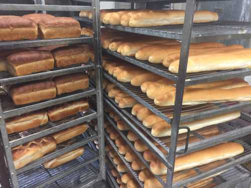 Racks filled with various types of freshly baked bread loaves, including sandwich and dinner rolls.