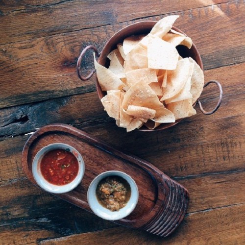 A wooden bowl filled with tortilla chips next to two small bowls of salsa on a wooden table.