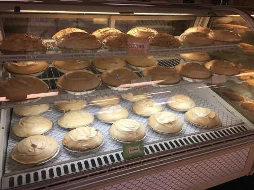 A display case filled with various pies, including coconut and lemon, topped with whipped cream.