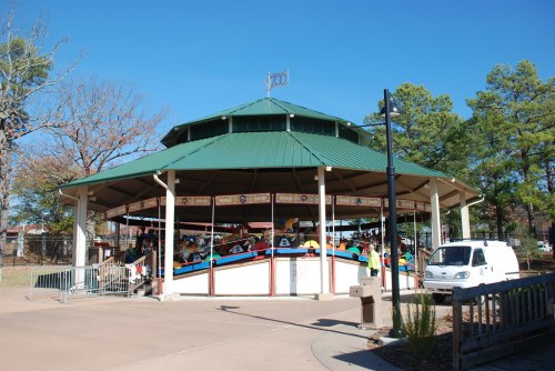A colorful carousel under a green roof, surrounded by trees and a clear blue sky.