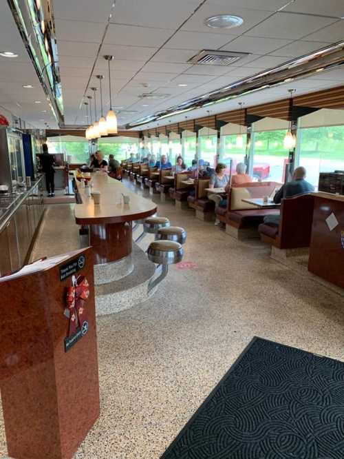 A retro diner interior with a long counter, booths, and large windows, featuring patrons enjoying their meals.