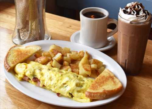 A plate with an omelette, golden toast, diced potatoes, a cup of coffee, and a chocolate milkshake topped with whipped cream.