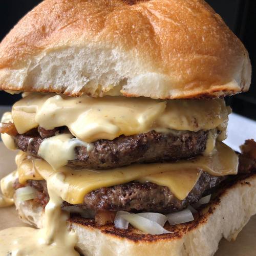 A close-up of a juicy double cheeseburger with melted cheese, onions, and a toasted bun.