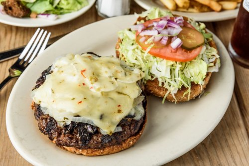 A plate with a burger patty topped with melted cheese, alongside a bun with lettuce, tomato, and onions.