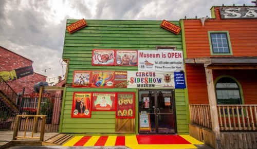 Colorful exterior of a circus sideshow museum with vintage posters and a sign indicating the museum is open.