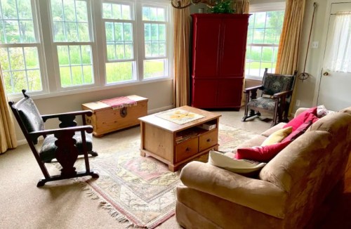 Cozy living room with a sofa, rocking chairs, coffee table, and large windows overlooking greenery.