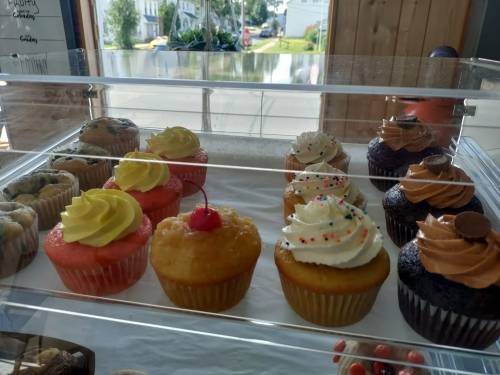 A display case filled with colorful cupcakes, featuring various frosting styles and toppings like sprinkles and cherries.