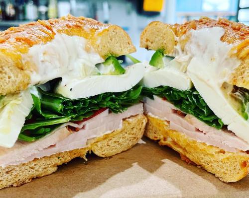 A close-up of a sandwich with turkey, lettuce, green peppers, and mozzarella on whole grain bread, cut in half.