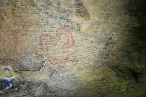 Ancient cave painting of a stylized animal figure on a rocky surface.