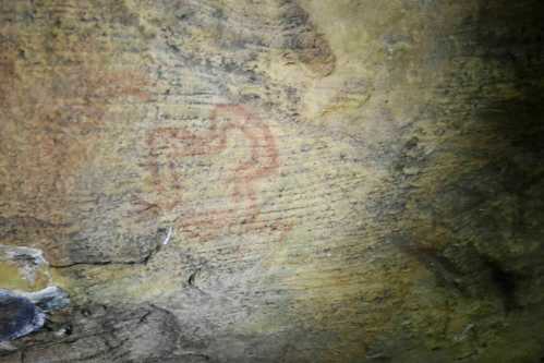 Ancient cave painting of a stylized animal figure on a rocky surface.