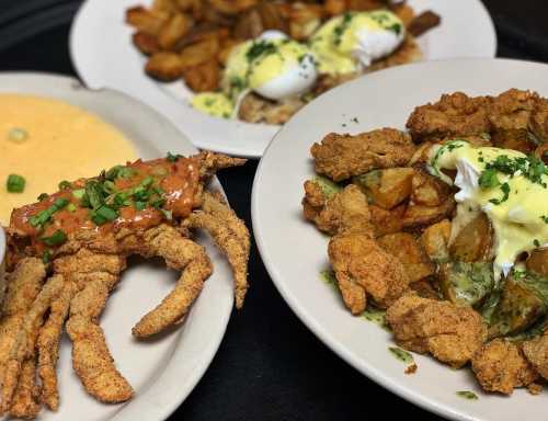 A plate featuring fried crab, poached eggs on potatoes, and a side of creamy grits, garnished with herbs.