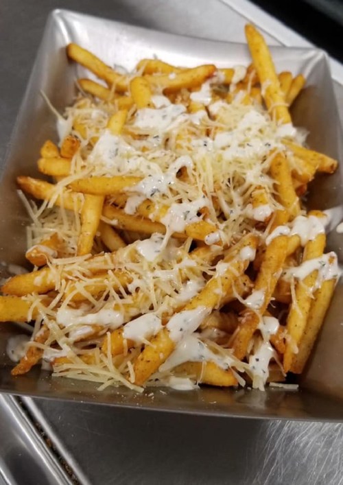 A metal tray filled with golden fries topped with creamy sauce and grated cheese.