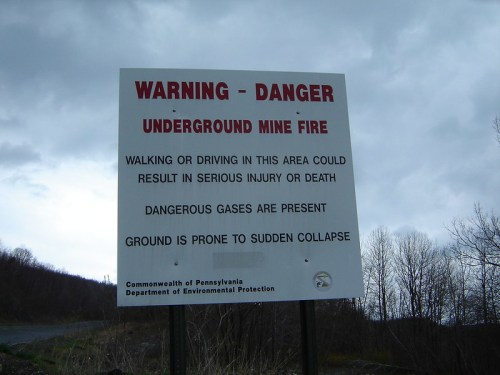 Sign warning of underground mine fire hazards, including risks of injury, dangerous gases, and ground collapse.