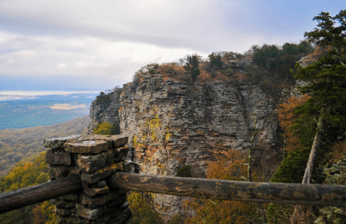 Scenic view of a rocky cliff with autumn foliage and a cloudy sky in the background.