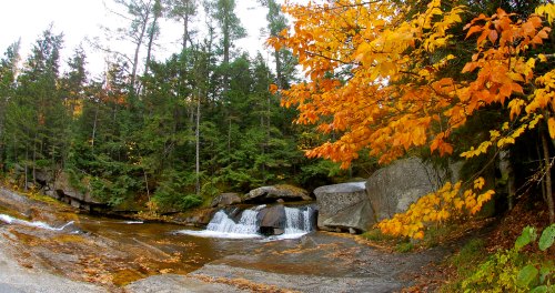A serene waterfall surrounded by autumn foliage and rocky terrain, with vibrant orange and yellow leaves.