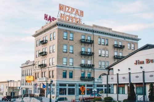 Historic Mizpah Hotel with a neon sign, featuring balconies and nearby shops in a charming town setting.