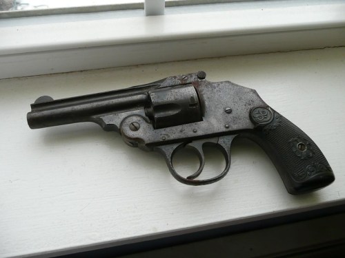 An old, rusty revolver rests on a white windowsill, showcasing its worn metal and textured grip.