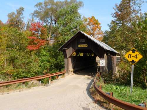 A wooden covered bridge surrounded by colorful autumn trees, with a warning sign for low clearance.