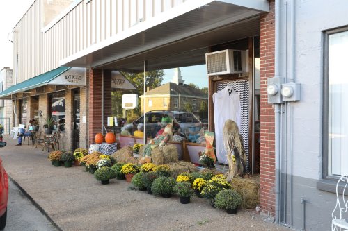A storefront decorated with pumpkins, hay bales, and colorful mums for fall, with outdoor seating visible.