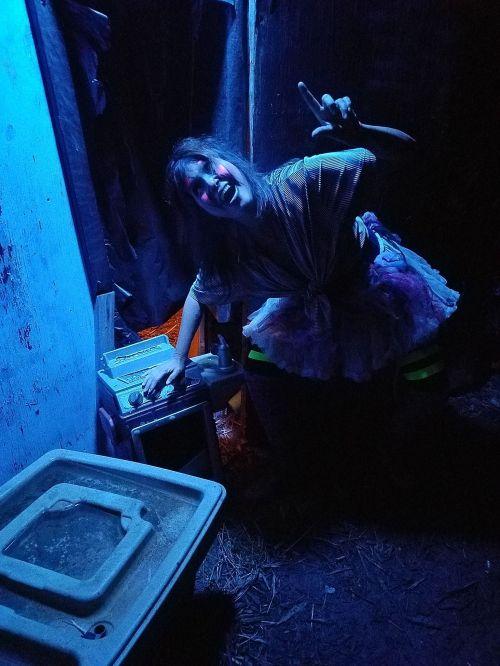 A person in a spooky setting, wearing a costume and striking a playful pose next to an old appliance, illuminated by blue light.