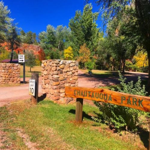 Entrance to Chautauqua Park with a stone sign, speed limit sign, and vibrant greenery under a clear blue sky.
