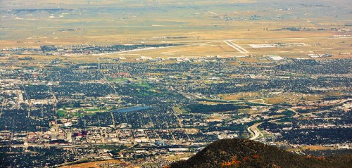 Aerial view of a city with an airport, green parks, and surrounding landscape under a clear sky.