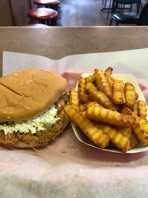 A pulled chicken sandwich with coleslaw beside a serving of crinkle-cut fries on a tray.