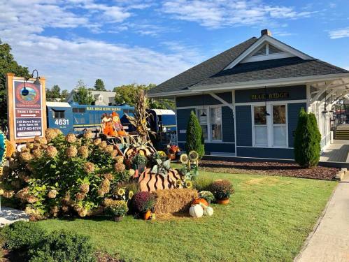 A charming blue building with a decorative fall display featuring pumpkins, sunflowers, and hay bales in front.