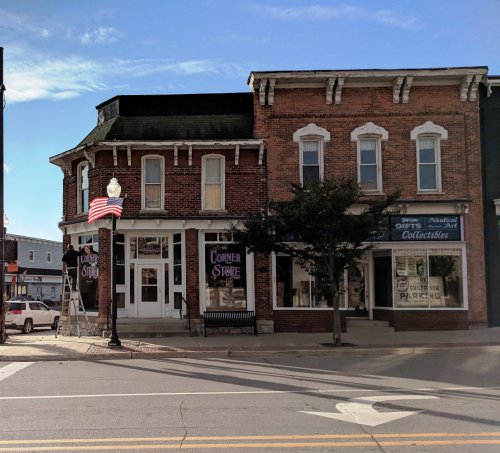 A brick building with a "Corner Store" sign, featuring large windows and a flagpole, set against a clear blue sky.