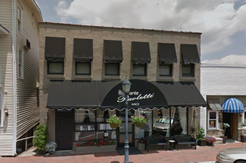 A restaurant with a black awning and outdoor seating, located in a charming town with a cloudy sky above.