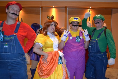 A group of people in colorful costumes, including Mario, Luigi, Wario, and Princess Daisy, posing together at an event.