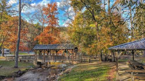 A scenic view of a wooden bridge over a stream, surrounded by colorful autumn trees and a picnic area.