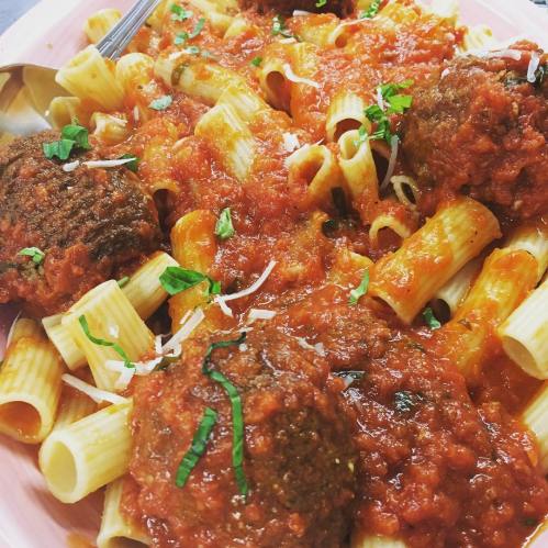 A plate of rigatoni pasta topped with marinara sauce, meatballs, and garnished with fresh basil and grated cheese.