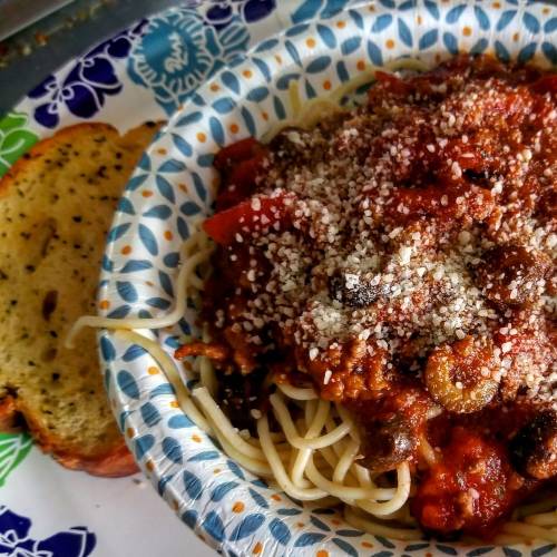 A plate of spaghetti topped with marinara sauce and grated cheese, alongside a slice of garlic bread.