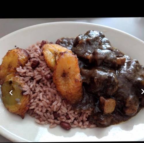 A plate of rice and beans served with fried plantains and a rich, dark sauce with chunks of meat.
