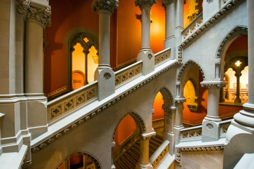 Intricate staircase with arches and columns, featuring warm orange walls and elegant architectural details.