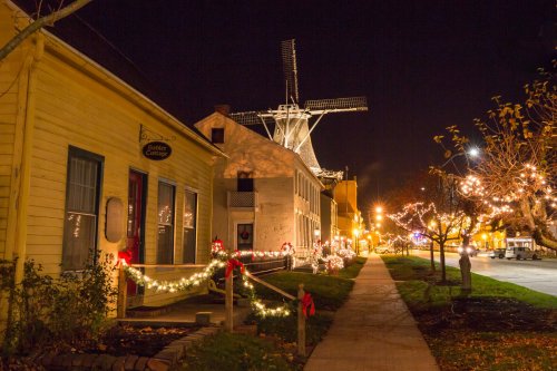 A charming street at night, lined with festive lights and decorations, featuring a windmill in the background.